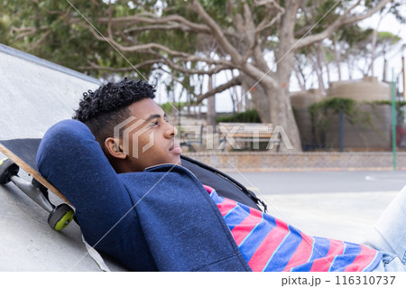 Relaxing at skatepark, teenage boy lying on skateboard, enjoying leisure time 116310737