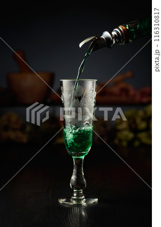 Green herbal liquor is poured from a vintage bottle into a glass. 116310817