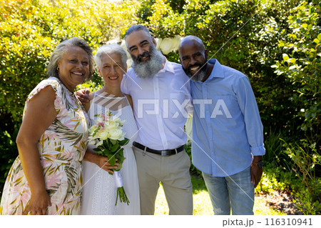 Smiling senior friends posing together outdoors, holding bouquet of flowers 116310941