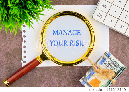 Manage your Risks symbol. Concept words Manage your Risks through a magnifying glass in a composition with American dollars, a calculator and a plant 116312540