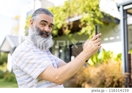 Taking selfie, senior man smiling and holding smartphone outside 116314159