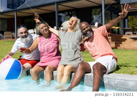 Group of senior friends sitting by pool, laughing and enjoying drinks together 116314221
