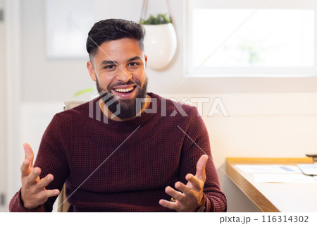 Smiling man gesturing while sitting at home, enjoying casual conversation, on video call Smiling man gesturing while sitting at home, enjoying casual conversation, on video call 116314302