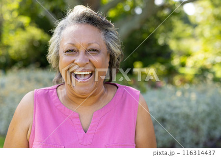 Smiling senior woman enjoying outdoor park, wearing pink sleeveless top Smiling senior woman enjoying outdoor park, wearing pink sleeveless top 116314437