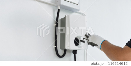A man electrician installing a home charging, installing charging station for electric car at private house A man electrician installing a home charging, installing charging station for electric car at private house 116314612