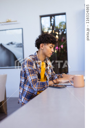 Writing in notebook, teenage boy sitting at table with smartphone and mug 116314865