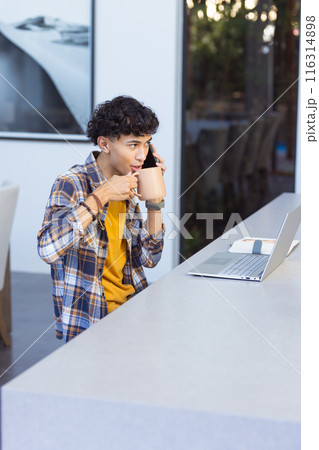 Talking on smartphone and drinking coffee, teenage boy working on laptop at home, copy space Talking on smartphone and drinking coffee, teenage boy working on laptop at home, copy space 116314898