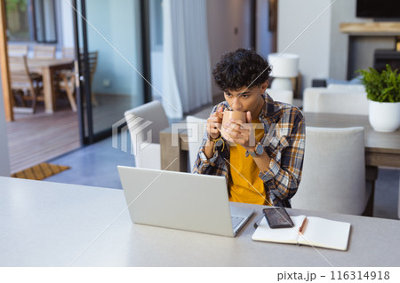 Drinking coffee, teenage boy using laptop and smartphone at home office 116314918