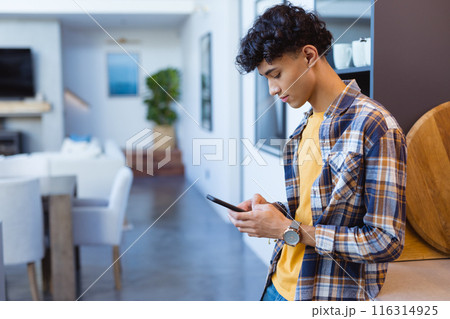 Using smartphone, teenage boy standing in modern home, focusing on screen, copy space 116314925
