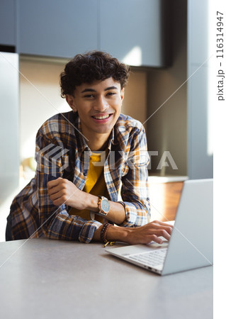 Smiling teenage boy using laptop at home, wearing plaid shirt and watch Smiling teenage boy using laptop at home, wearing plaid shirt and watch 116314947