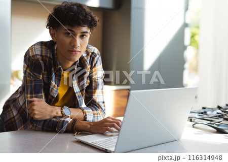 Using laptop, teenage boy in casual attire working from home kitchen, copy space 116314948