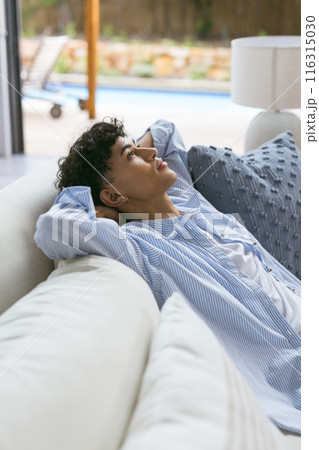 Relaxing on couch, teenage boy in striped shirt looking thoughtful at home 116315030