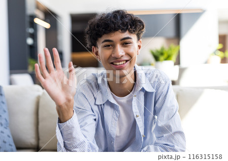 Smiling teenage boy waving hand while sitting on couch at home Smiling teenage boy waving hand while sitting on couch at home 116315158