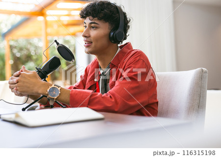 Recording podcast, young man in red shirt speaking into microphone with headphones Recording podcast, young man in red shirt speaking into microphone with headphones 116315198