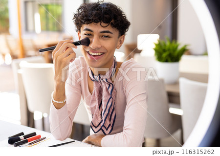 Applying makeup with brush, transgender woman smiling and sitting at table Applying makeup with brush, transgender woman smiling and sitting at table 116315262