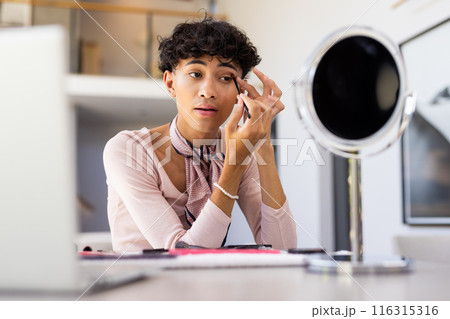 Applying makeup, transgender transgender woman using mirror at home, focusing on details 116315316