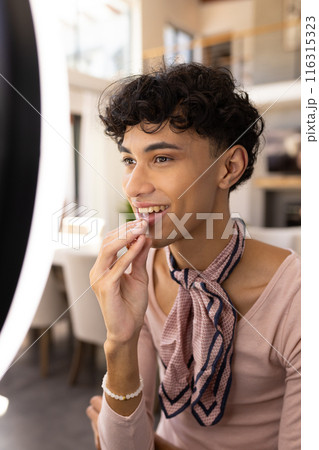 Applying lipstick, transgender transgender woman smiling and looking in mirror at home 116315323