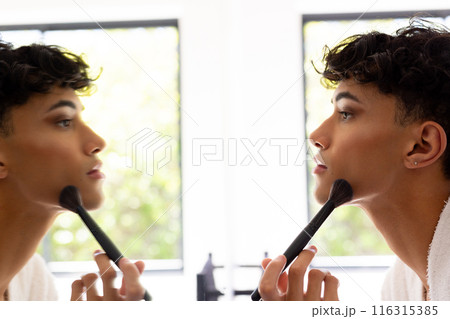 Applying makeup, transgender woman using brush and looking in mirror at home 116315385