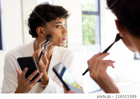 Applying makeup, transgender woman using smartphone while looking in mirror Applying makeup, transgender woman using smartphone while looking in mirror 116315389