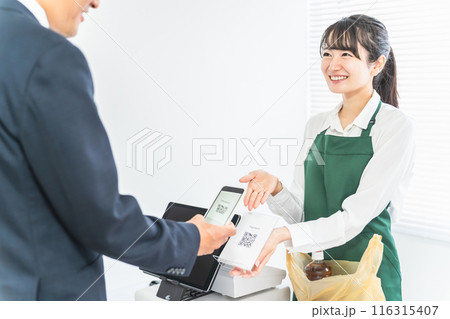 コンビニでスマホ・QRコード決済を案内する女性店員と買い物客のサラリーマン男性 116315407
