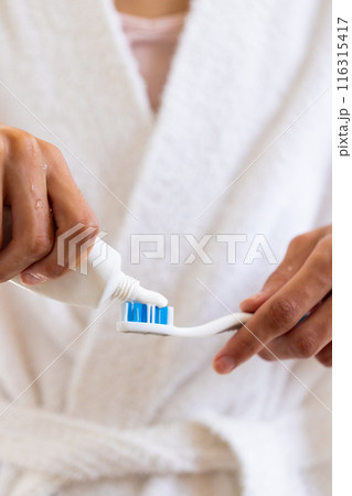 Applying toothpaste on toothbrush, young man in bathrobe preparing for brushing teeth 116315417