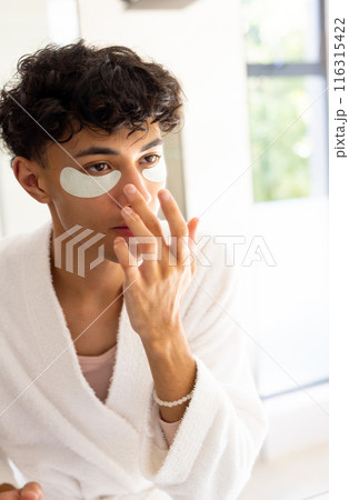 Applying skincare, young young man with eye patches in bathroom, wearing bathrobe Applying skincare, young young man with eye patches in bathroom, wearing bathrobe 116315422