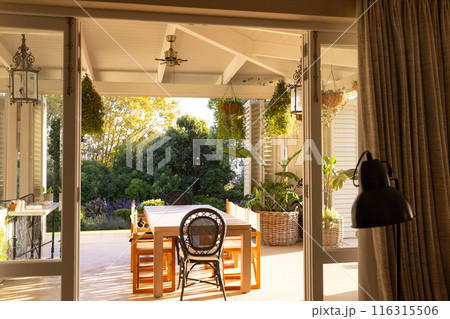 Sunlight illuminating cozy patio with dining table and hanging plants, copy space 116315506