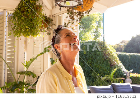 Smiling mature woman enjoying sunny day in cozy home garden patio Smiling mature woman enjoying sunny day in cozy home garden patio 116315512