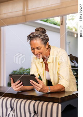 Standing at home, mature woman using tablet and smiling Standing at home, mature woman using tablet and smiling 116315527