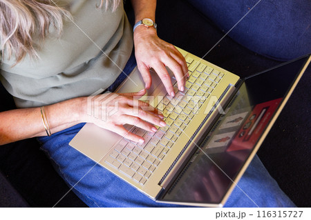 Typing on laptop, mature woman working from home on couch in casual attire Typing on laptop, mature woman working from home on couch in casual attire 116315727