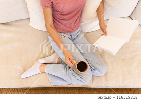 Reading book and holding coffee cup, woman relaxing on couch at home 116315818