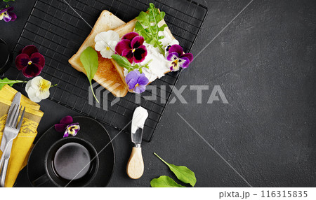 brioche toast with cream cheese and pansy flowers on a plate. Gourmet breakfast. Selective focus, black background, copy space brioche toast with cream cheese and pansy flowers on a plate. Gourmet breakfast. Selective focus, black background, copy space 116315835