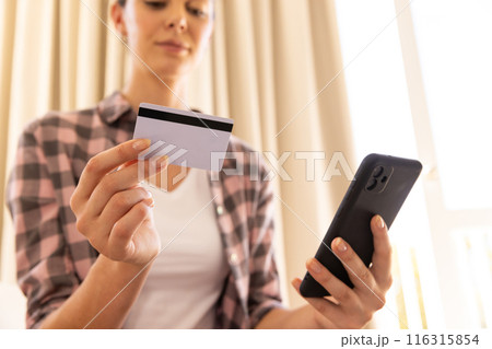 Holding credit card and smartphone, woman making online payment at home Holding credit card and smartphone, woman making online payment at home 116315854