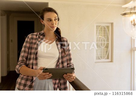 Holding tablet, woman standing in hallway, looking thoughtful 116315868