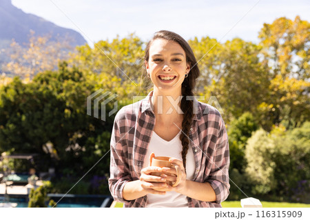 Smiling woman holding coffee cup, enjoying outdoor view at home 116315909