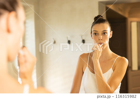 Brushing teeth, young woman looking in mirror in bathroom at home 116315982