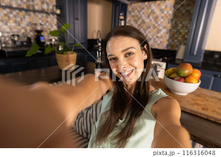 Taking selfie, woman smiling in kitchen with fruit bowl on counter Taking selfie, woman smiling in kitchen with fruit bowl on counter 116316048