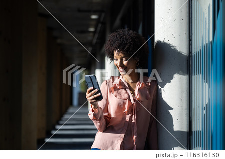 Leaning on column, smiling woman using smartphone for business communication outdoors, copy space Leaning on column, smiling woman using smartphone for business communication outdoors, copy space 116316130