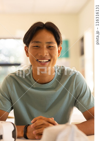 Smiling teenage boy sitting at high school desk, looking at camera in classroom 116316131