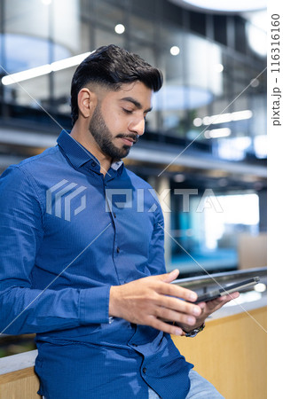 Using tablet, man in blue shirt working in modern office environment Using tablet, man in blue shirt working in modern office environment 116316160