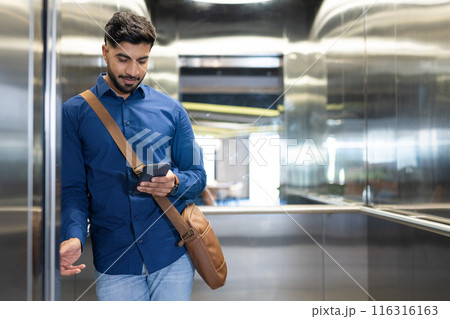 Using smartphone, man with messenger bag standing in elevator, checking messages, copy space Using smartphone, man with messenger bag standing in elevator, checking messages, copy space 116316163