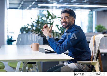 Smiling businessman sitting at desk with tablet and coffee mug in office, copy space 116316208