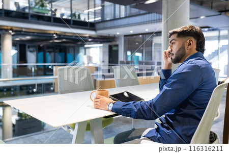 Talking on smartphone, man holding coffee cup and sitting in modern office, copy space 116316211