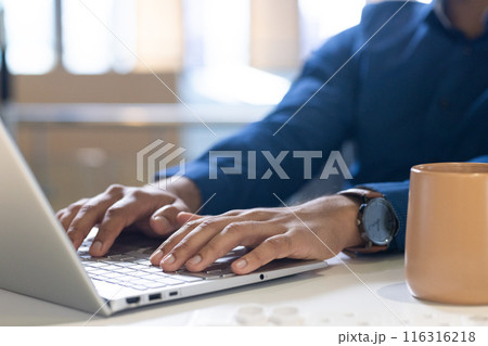 Typing on laptop, man working in office with coffee mug on desk 116316218