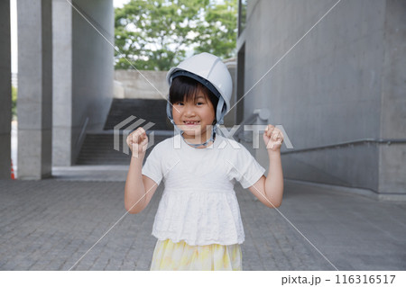 ヘルメットをかぶった笑顔の小学生がガッツポーズをする。頑丈な建物と防災訓練 116316517