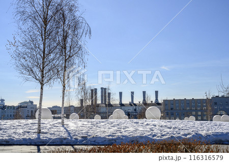 Snowy field with white balls and a birch tree on the background of hydroelectric power plant pipes 116316579