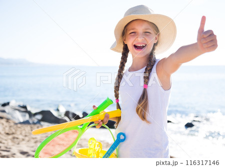 Child in hat on beach shows thumb up 116317146
