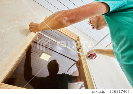 Measuring doorway to mark using tape measure holding piece in place and marking where it needs to be cut with pencil. 116317405