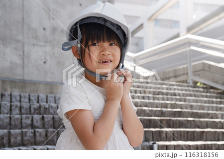 コンクリート建物背景にヘルメットをかぶった小学生の女の子 116318156