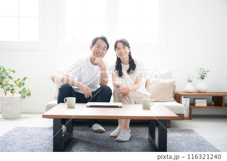 明るい綺麗なリビングでパソコンを見ながら話し合う50代夫婦のカメラ目線 116321240